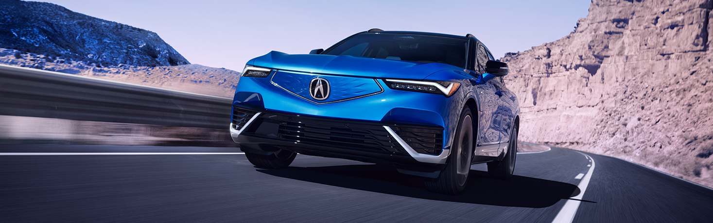 Blue Acura electric car driving down highway.