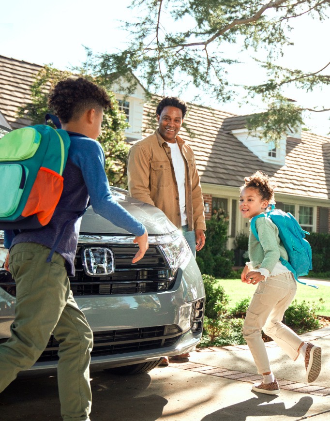 Kids and dad arriving home in Honda Odyssey van with mom in background.